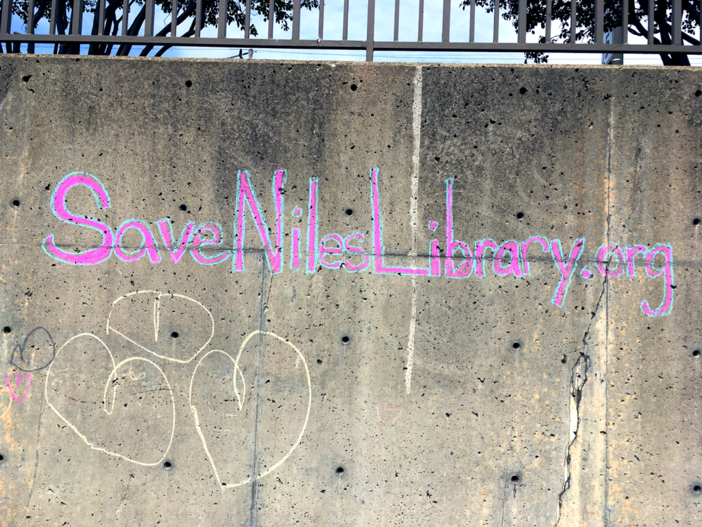 Chalk on a wall that reads # Save Niles Library.