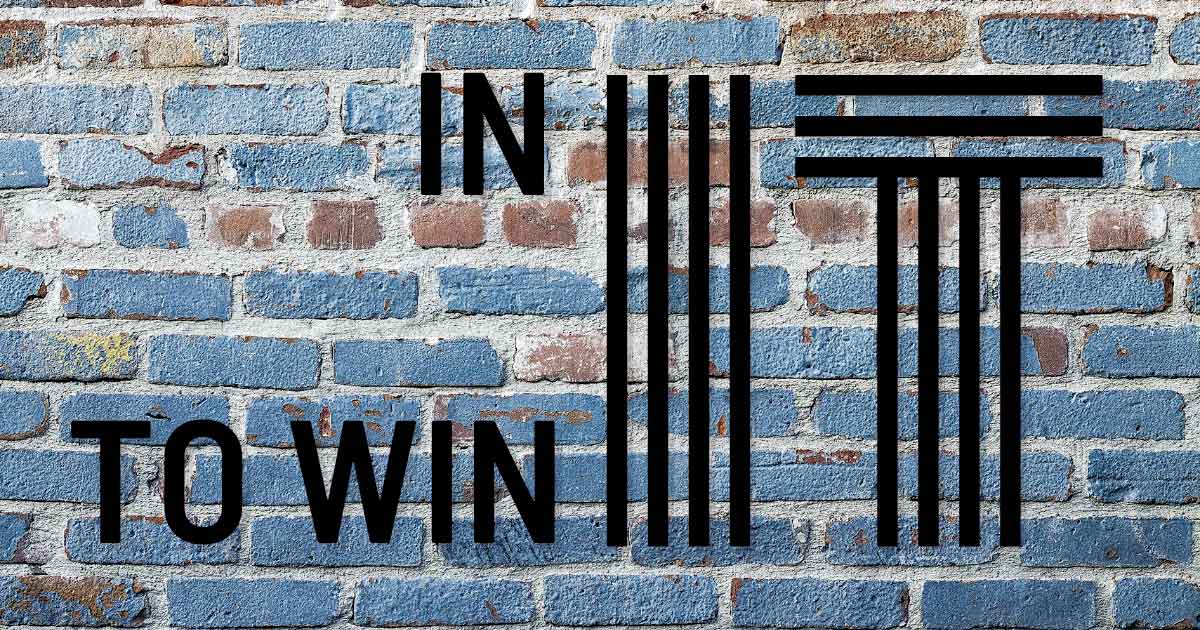 A blue painted brick wall with the words In It To Win It overlaid.