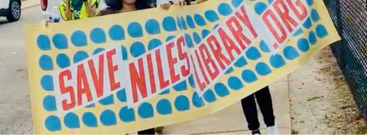 A banner at a rally being carried by several people that reads "Save Niles Library .org"
