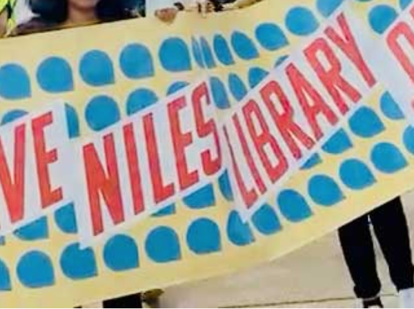 A banner at a rally being carried by several people that reads "Save Niles Library .org"